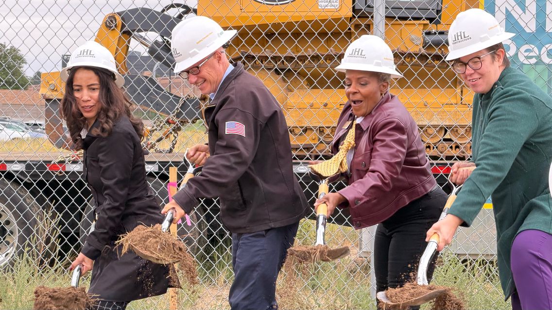 Participants wearing hard hats lift shovels of dirt at the groundbreaking.